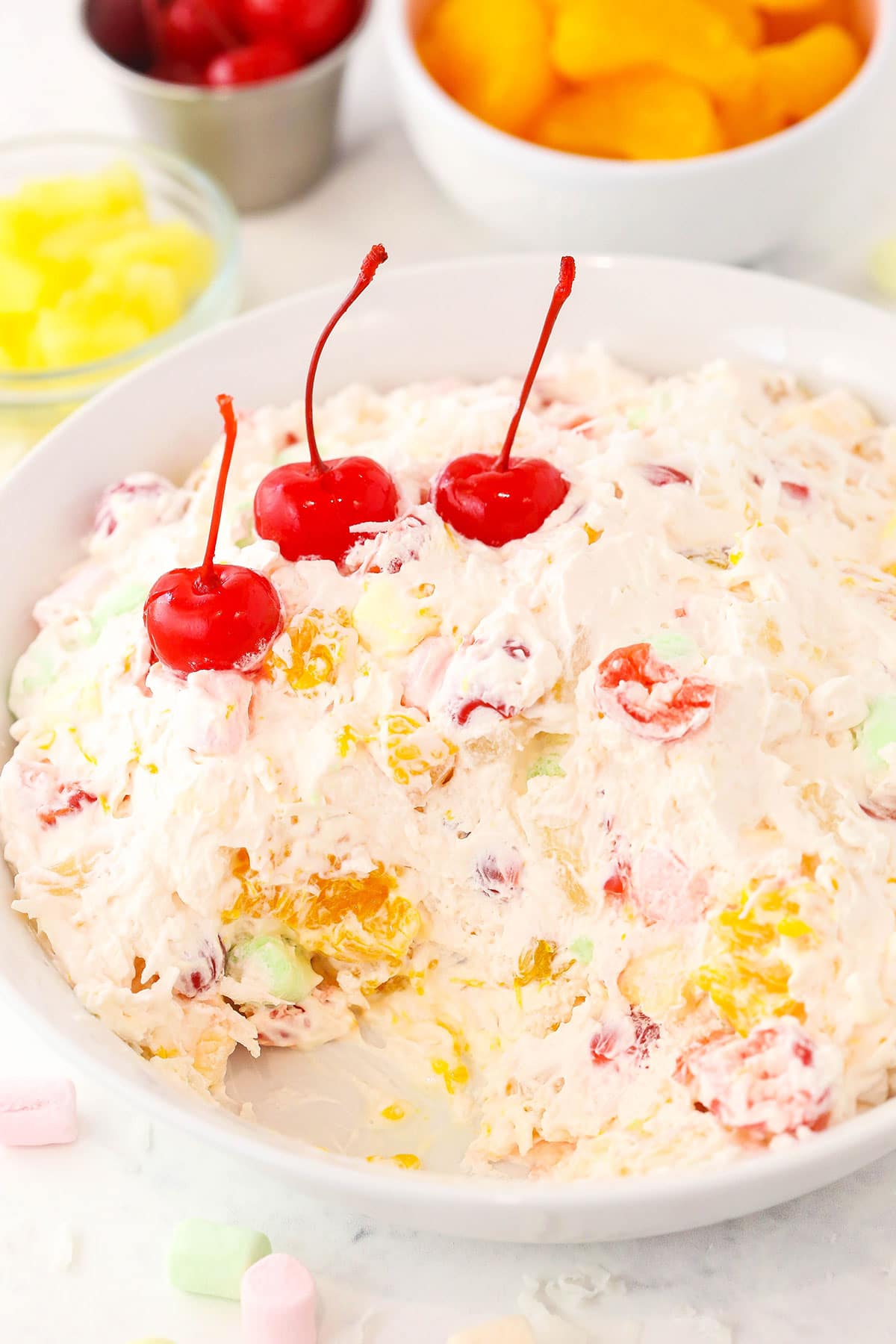 Maraschino cherries, tangerines and pineapple chunks are combined with a fluffy whipped cream dressing in this easy Ambrosia salad recipe! A serving platter filled with Cool Whip fruit salad with three maraschino cherries placed on top