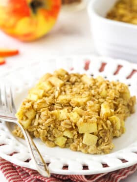A square of apple cinnamon baked oatmeal on a white plate on top of a red and white striped dishtowel