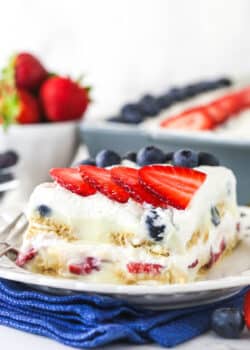 slice of berry icebox cake on white plate with blue napkin underneath and berries in the background