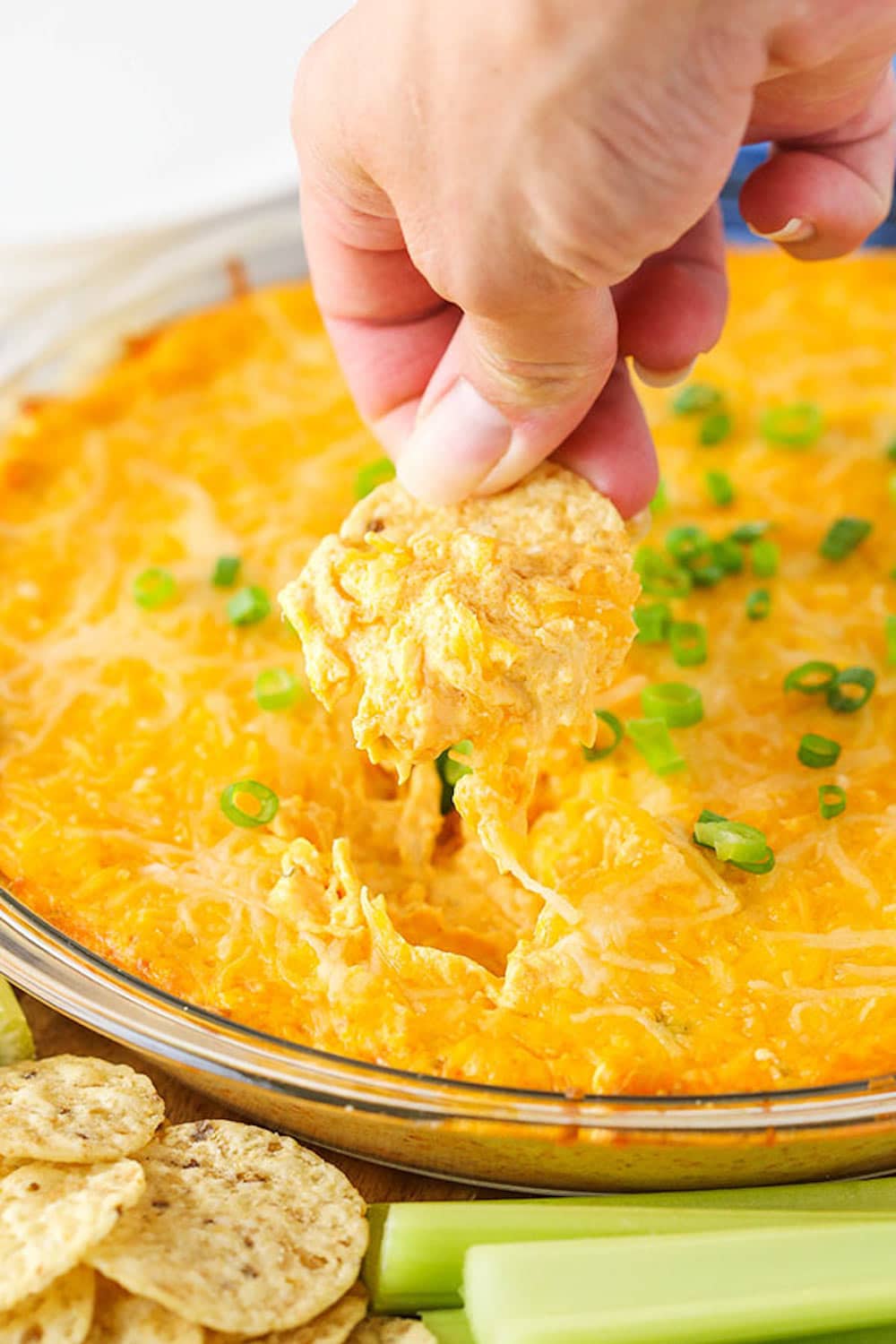 This easy Franks Buffalo Chicken Dip might be my favorite dip recipe of all time! It's cheesy & creamy with the perfect amount of spiciness. A chip scooping up some Cheesy Buffalo Dip from a clear bowl.