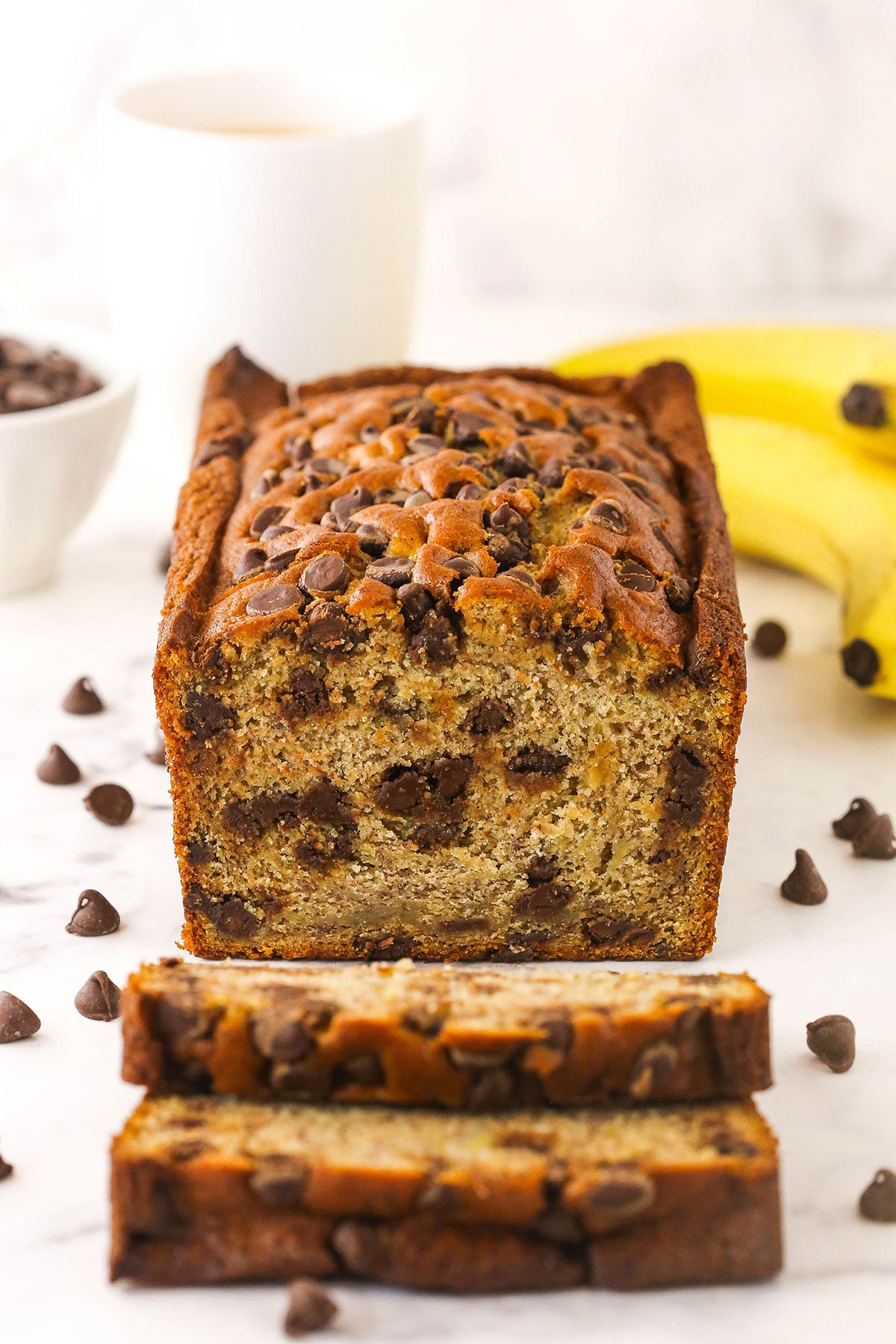 This easy Chocolate Chip Banana Bread has the moistest crumb & the softest, fluffiest texture. You'll never follow a different recipe again! A loaf of banana bread with two freshly cut slices in front of it