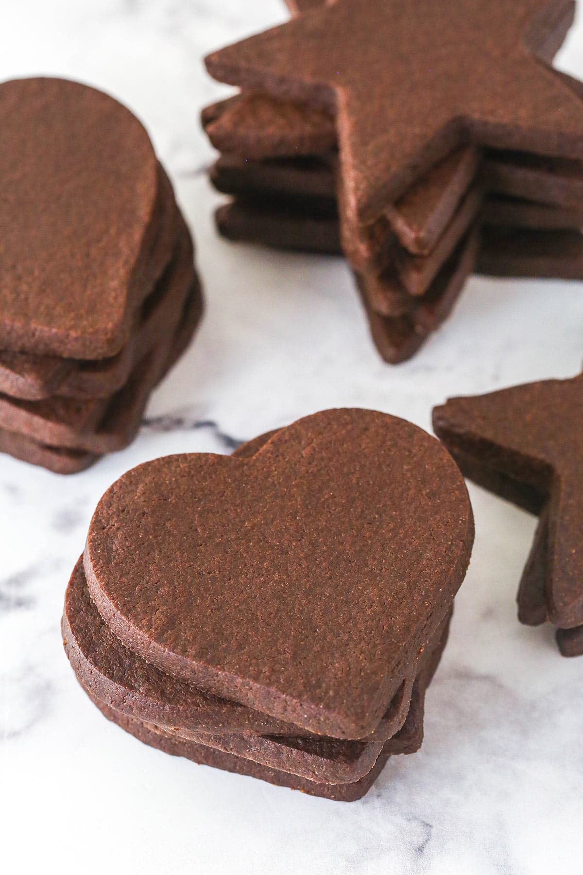 Perfectly soft and chewy, Chocolate Cut Out Cookies are easy cookies that the whole family will love. Decorate with your favorite icing. stacks of chocolate cutout cookies on marble counter