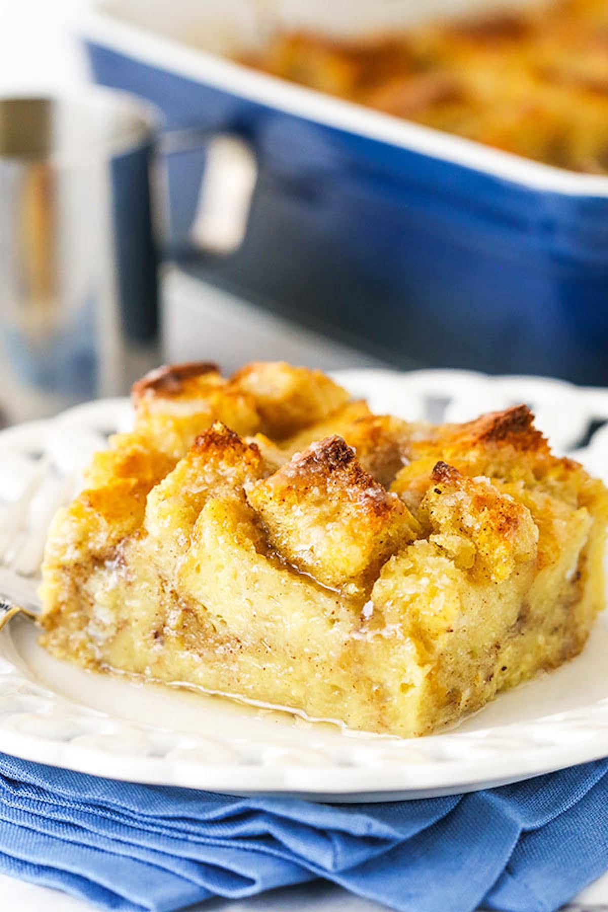 Old fashioned bread pudding just like grandma used to make! This easy recipe turns stale bread into a cozy pudding soaked in vanilla sauce. A single serving of bread pudding sitting on a plate on top of a blue napkin.
