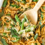 A wooden spoon scooping up a serving of green bean casserole from a ceramic baking dish.