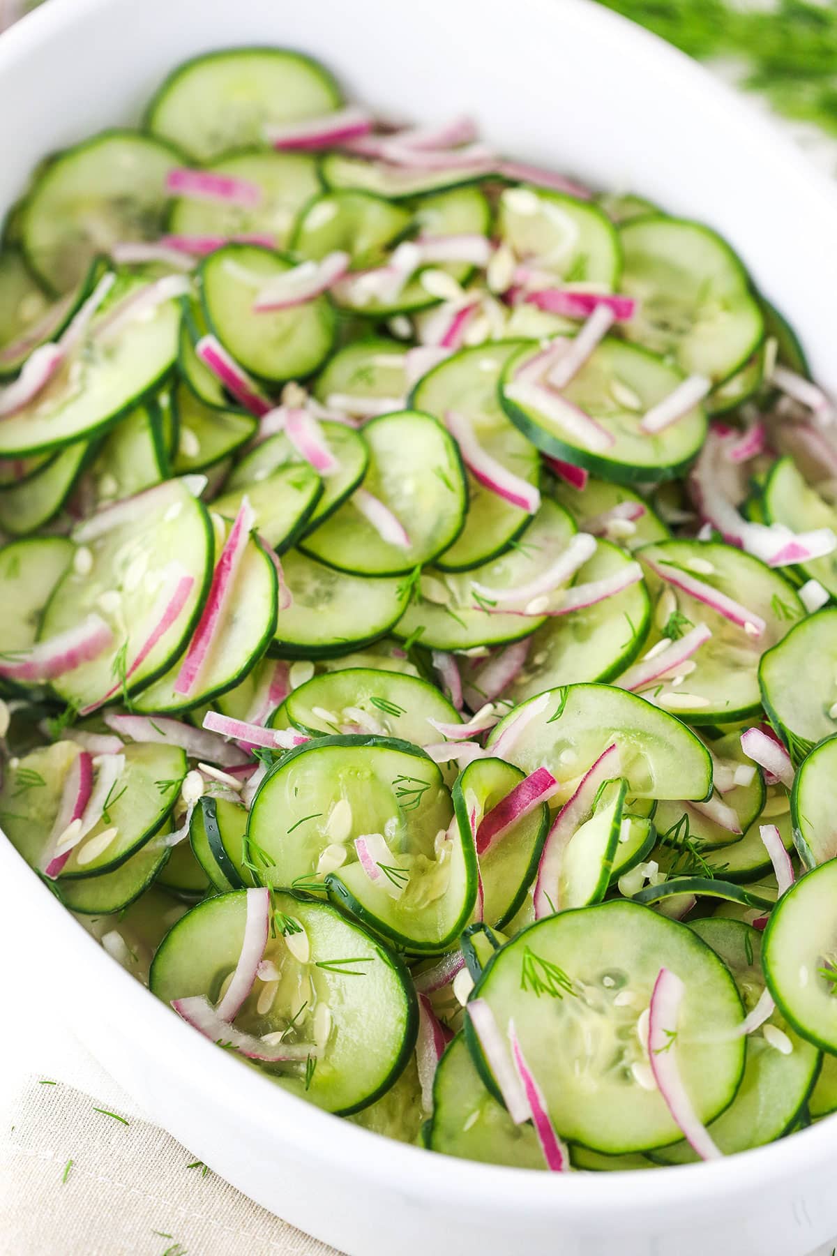 This Cucumber Salad is a long time favorite that's easy to make and hard to resist! Cucumbers and onion are tossed with a little sugar, vinegar and dill for a fresh, light side dish! cucumber salad in white dish - angled shot