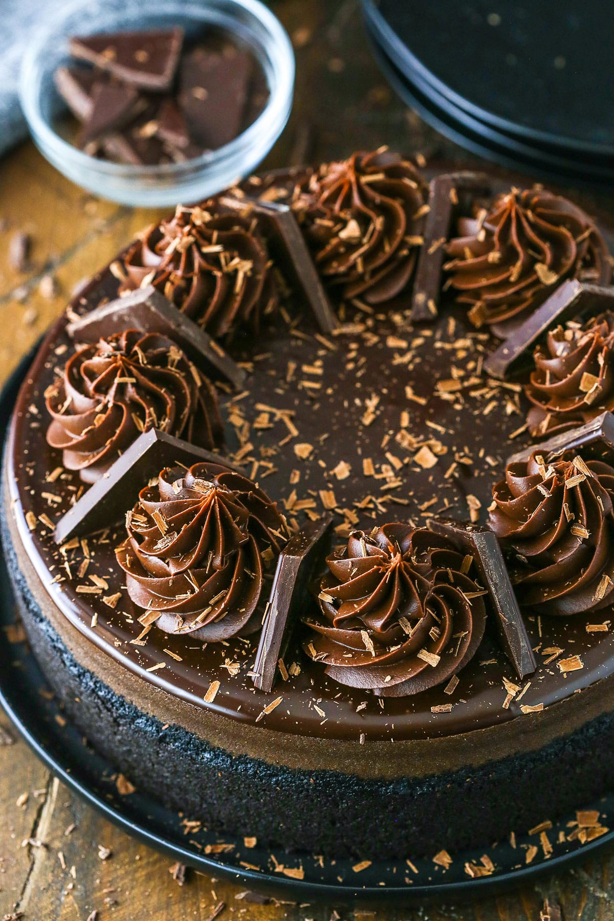 This Dark Chocolate Cheesecake recipe is rich, creamy and full of decadent dark chocolate! It's topped with a dark chocolate ganache and dark chocolate ganache swirls for the ultimate chocolate cheesecake! Overhead view of a full Decadent Dark Chocolate Cheesecake topped with dark chocolate ganache swirls and pieces of dark chocolate.