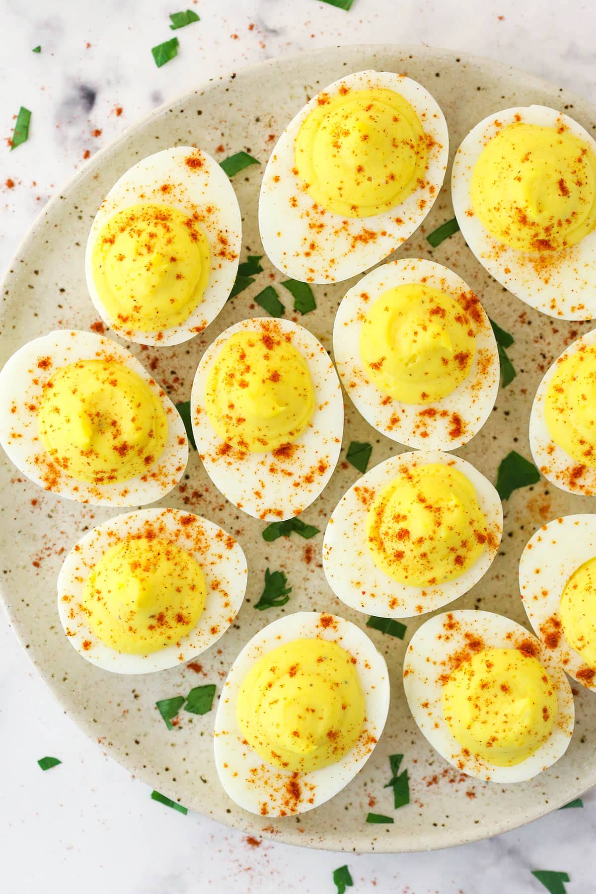 Deviled eggs are made of egg yolks mixed with mayo, mustard, salt, and pepper and piped back into their whites. Overhead image of deviled eggs on a serving plate.
