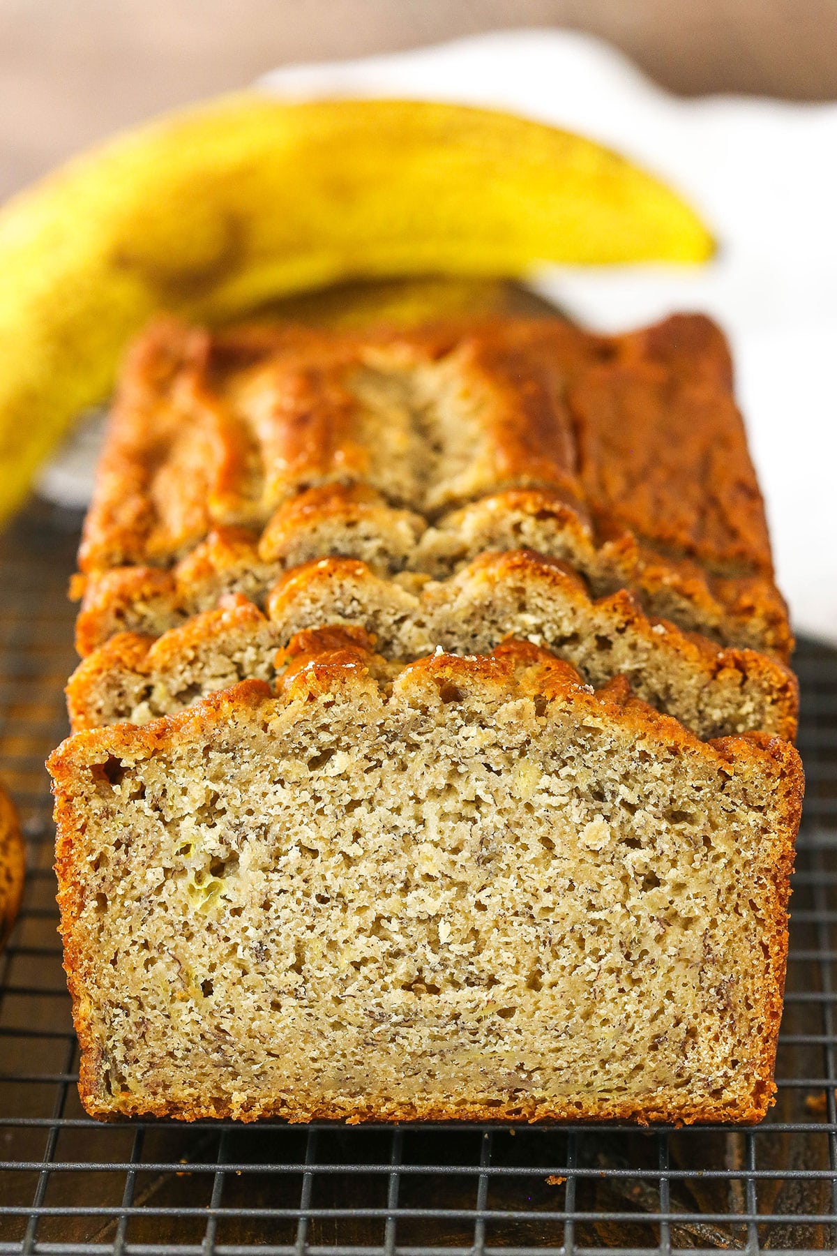 This Easy Banana Bread Recipe makes a moist loaf with TONS of banana flavor! You're going to love this classic banana bread that's perfect for all those over ripe bananas! Side view of three Banana Bread slices leaning against the remaining banana bread loaf on a cooling rack