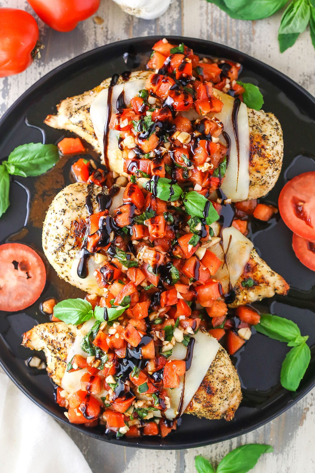 This Easy Bruschetta Chicken recipe is made with tender chicken breast pieces coated in garlic and spices that are grilled, then topped with a fresh tomato and basil topping. A little drizzle of balsamic glaze takes the flavors over the top! Overhead view of Bruschetta Chicken in a black pan