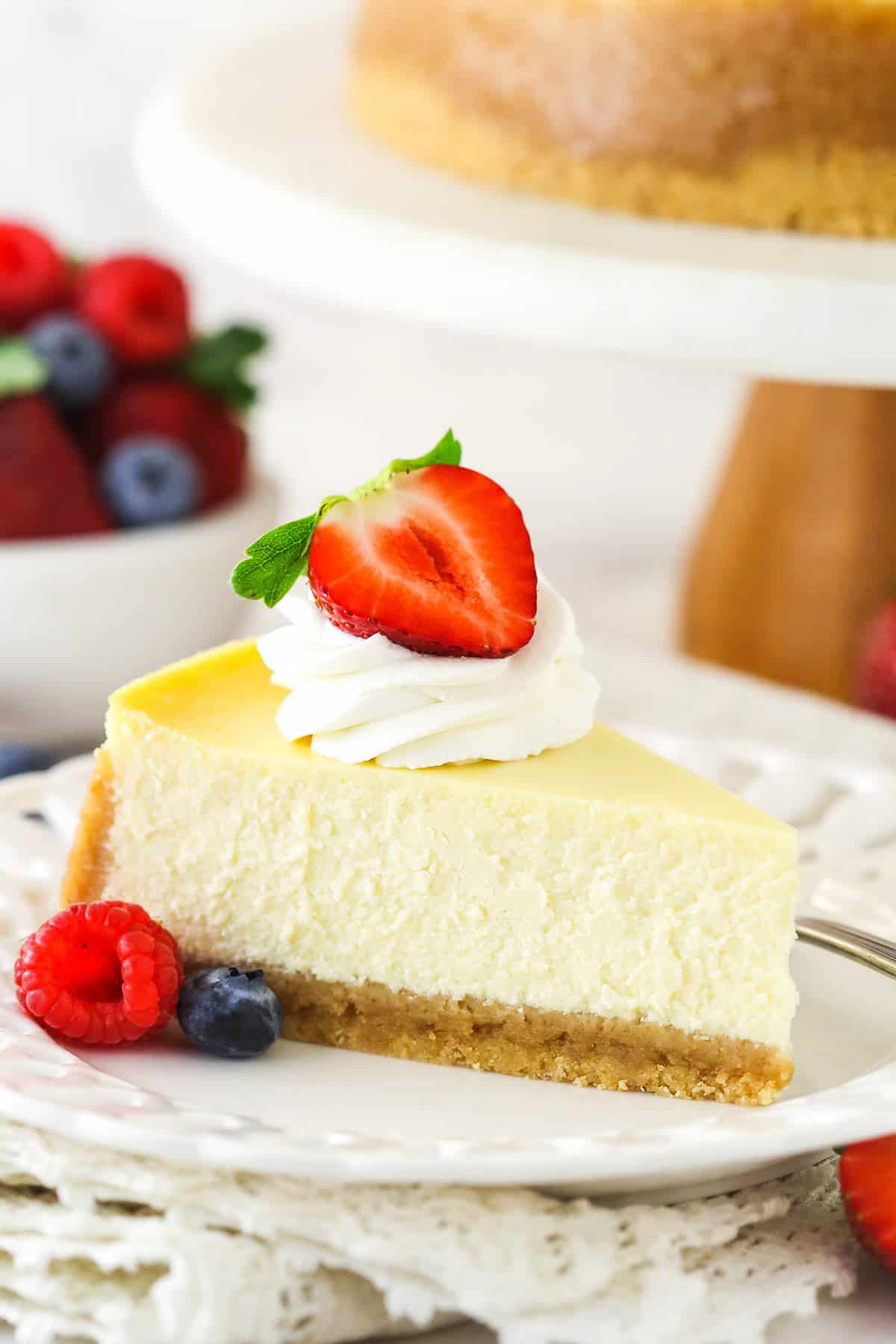 This easy cheesecake recipe makes a creamy, ultra-smooth cheesecake with vanilla wafer crust. Truly the best classic cheesecake you can make! A slice of homemade cheesecake with whipped cream and berries
