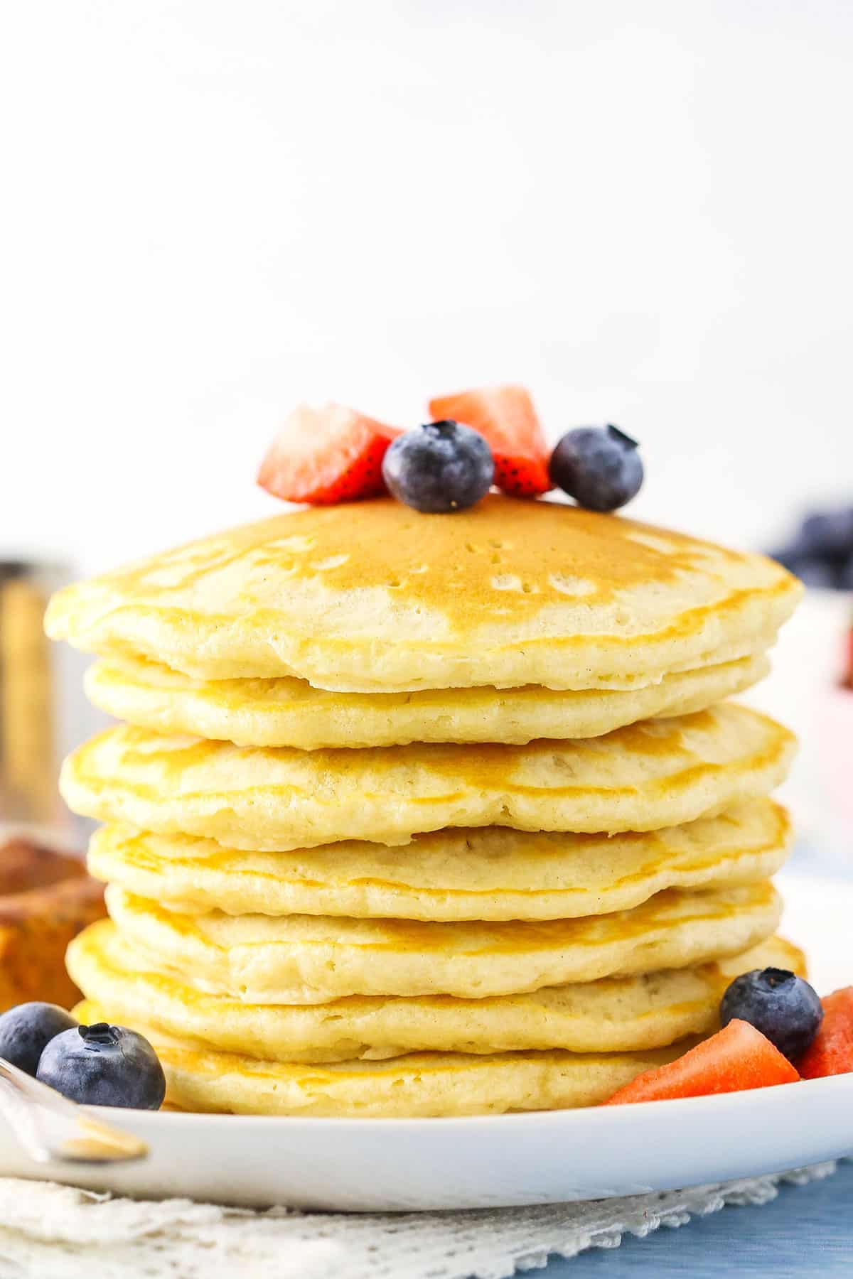 Side view of seven pancakes stacked on a white plate and topped with cut strawberries and blueberries