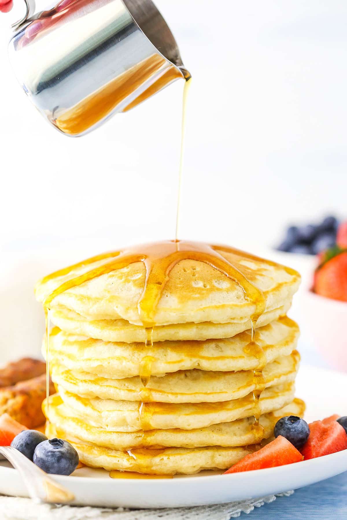Pouring syrup over seven pancakes stacked on a white plate