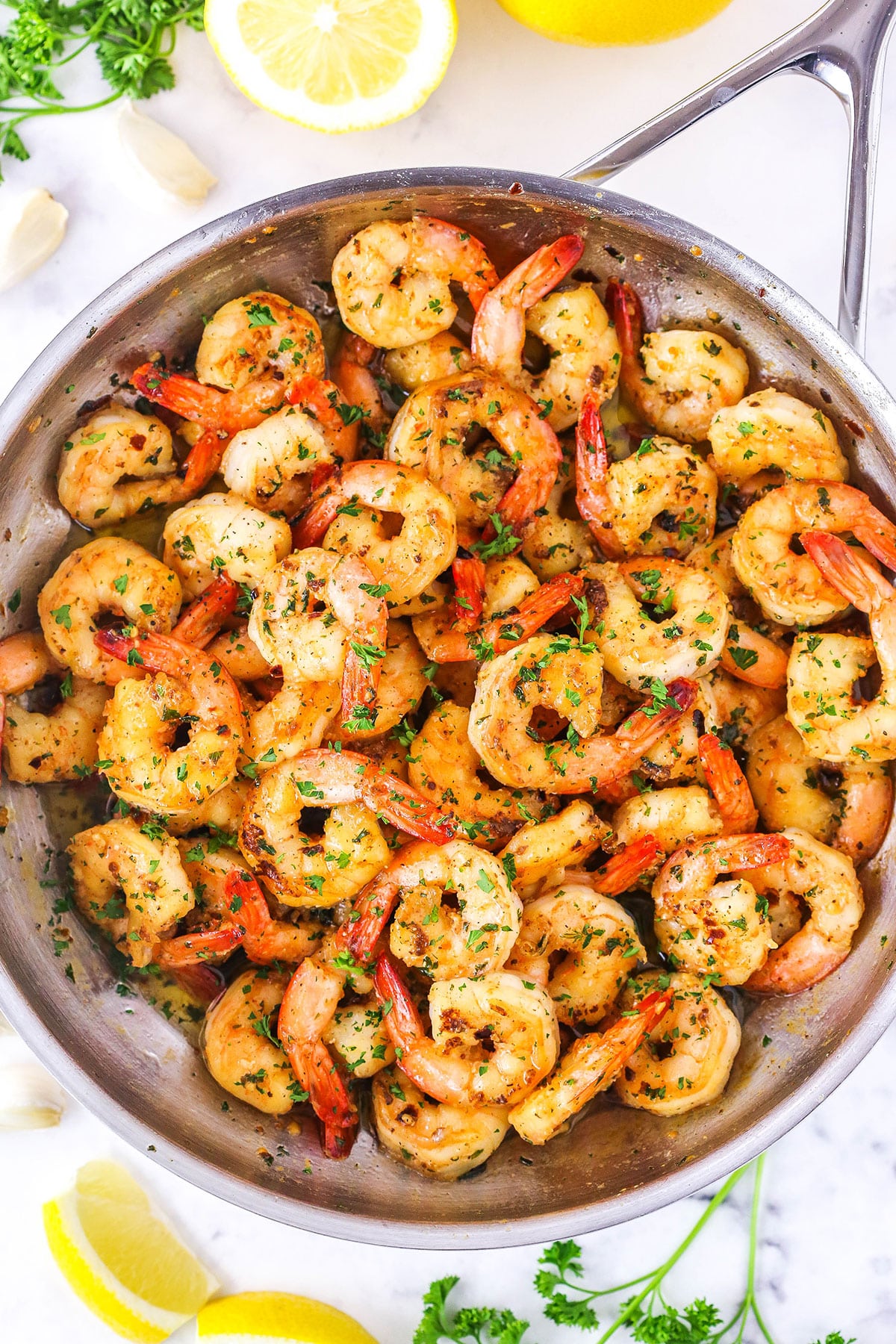This Garlic Butter Shrimp Scampi has an addicting garlic buttery sauce with a little lemon in it! Plus, you can have it ready to go in about 20 minutes! The perfect appetizer or quick dinner idea! Overhead view of Garlic Butter Shrimp Scampi in a metal pan with cut lemons in the background