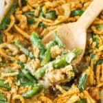 A wooden spoon scooping up a serving of green bean casserole from a ceramic baking dish.