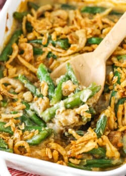 A wooden spoon scooping up a serving of green bean casserole from a ceramic baking dish.