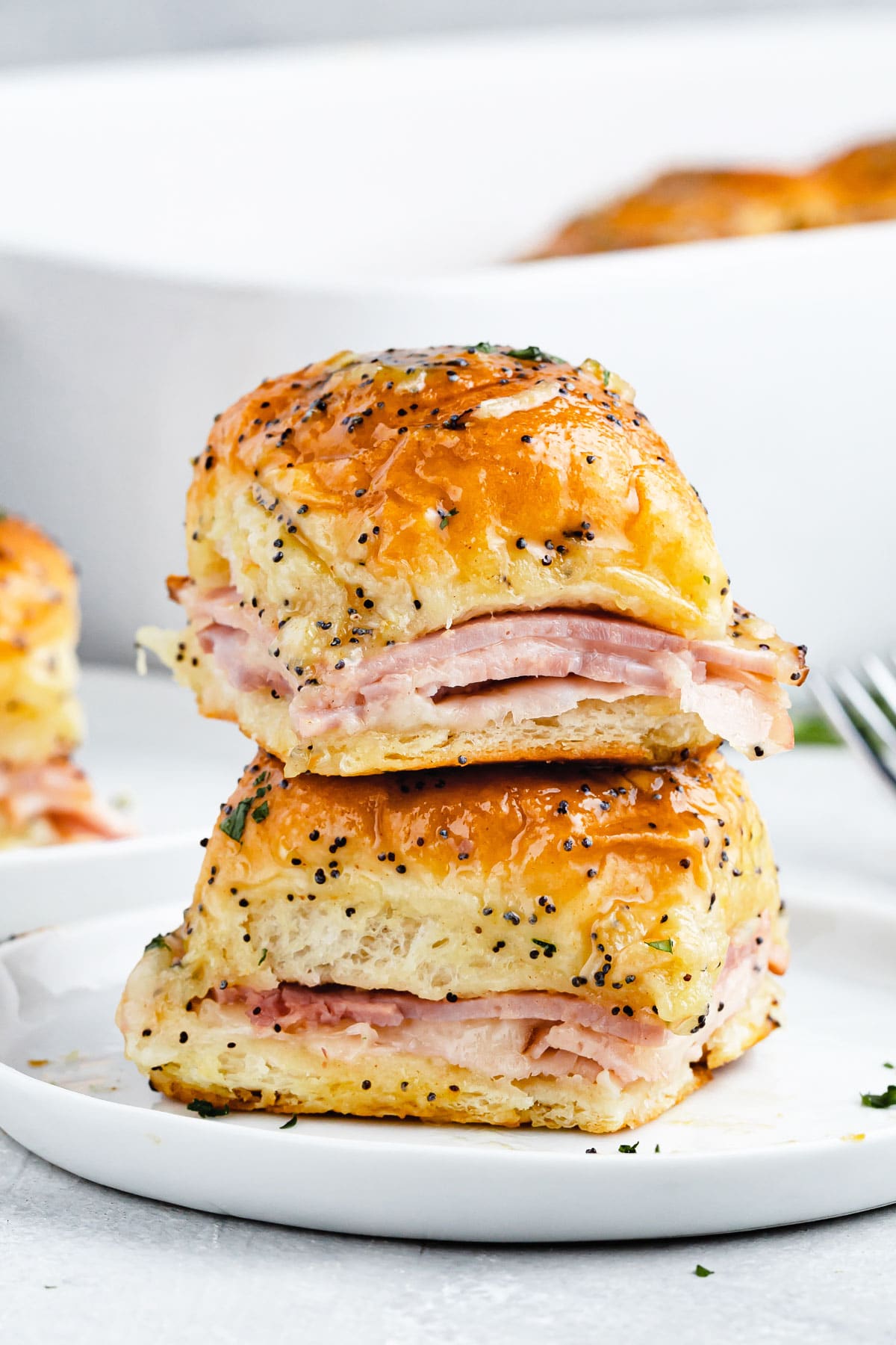 Two ham and cheese sliders stacked on top of one another on a plate