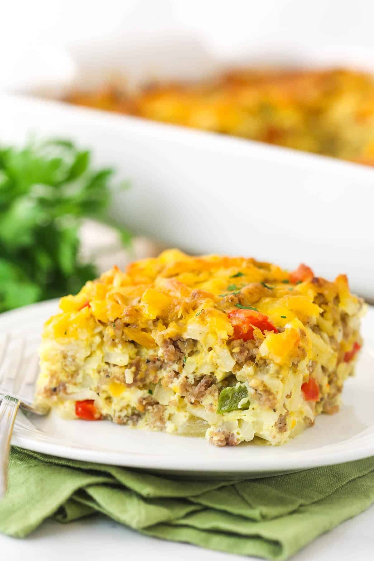 This Hashbrown Breakfast Casserole is perfect when you need to feed a crowd in the morning. Perfect for Christmas, Thanksgiving, or brunch! A piece of hashbrown breakfast casserole on a plate ready to be eaten