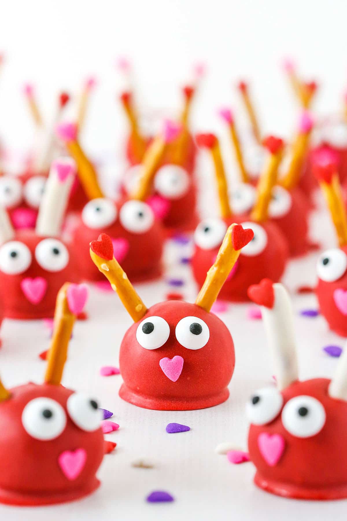 These Love Bug Oreo Cookie Balls are so fun for Valentine's Day and a great treat for sharing! Learn how to make them with simple ingredients - pretzels, eyeball candies and sprinkles! Love Bug Oreo Cookie Balls with pretzel sticks for feelers and heart noses displayed on a white marble table top