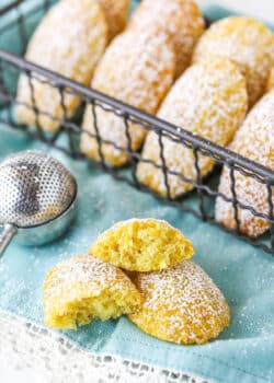 A Madeleine Tea Cake Broken in Half on a Teal Napkin with Other Cookies Nearby.