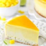 slice of mango key lime cheesecake on white plate with mango and limes in the background