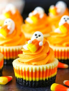 Mini Candy Corn Cheesecakes on a black table top surrounded by candy corn