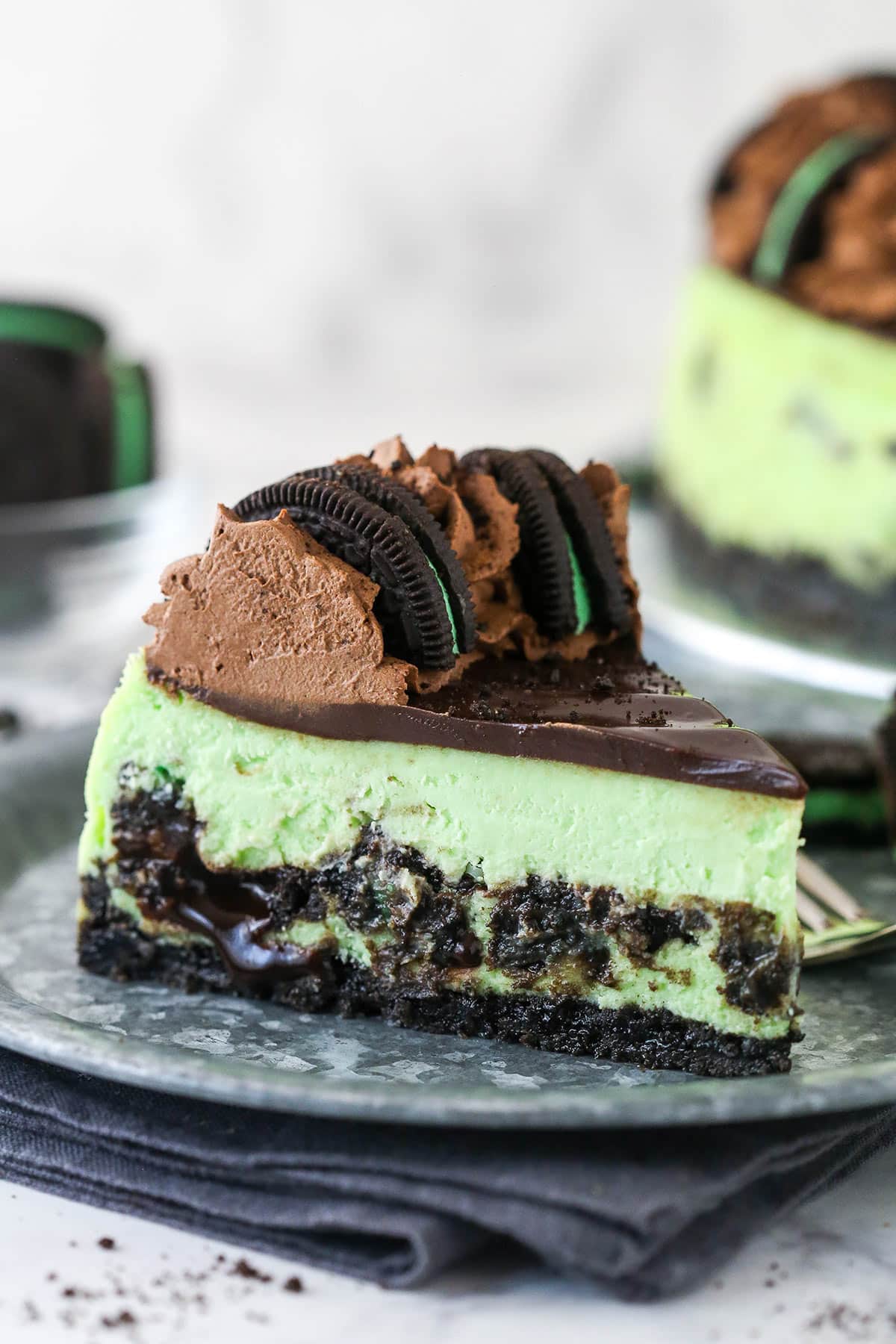 Mint Oreo cheesecake is made of mint Oreo crust, mint Oreo-loaded minty cheesecake filling, chocolate ganache, & chocolate whipped cream. A slice of mint Oreo cheesecake.