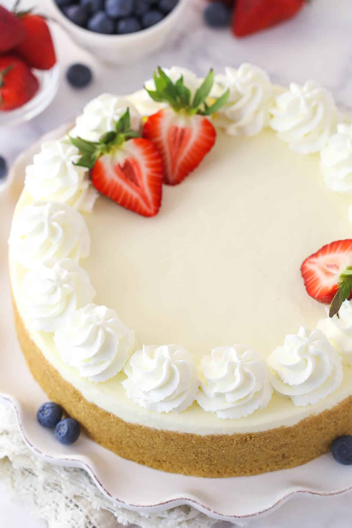 No-bake cheesecake is made up of smooth, creamy, vanilla filling over buttery graham cracker crust and is topped with homemade whipped cream. Overhead image of a no bake cheesecake garnished with berries.
