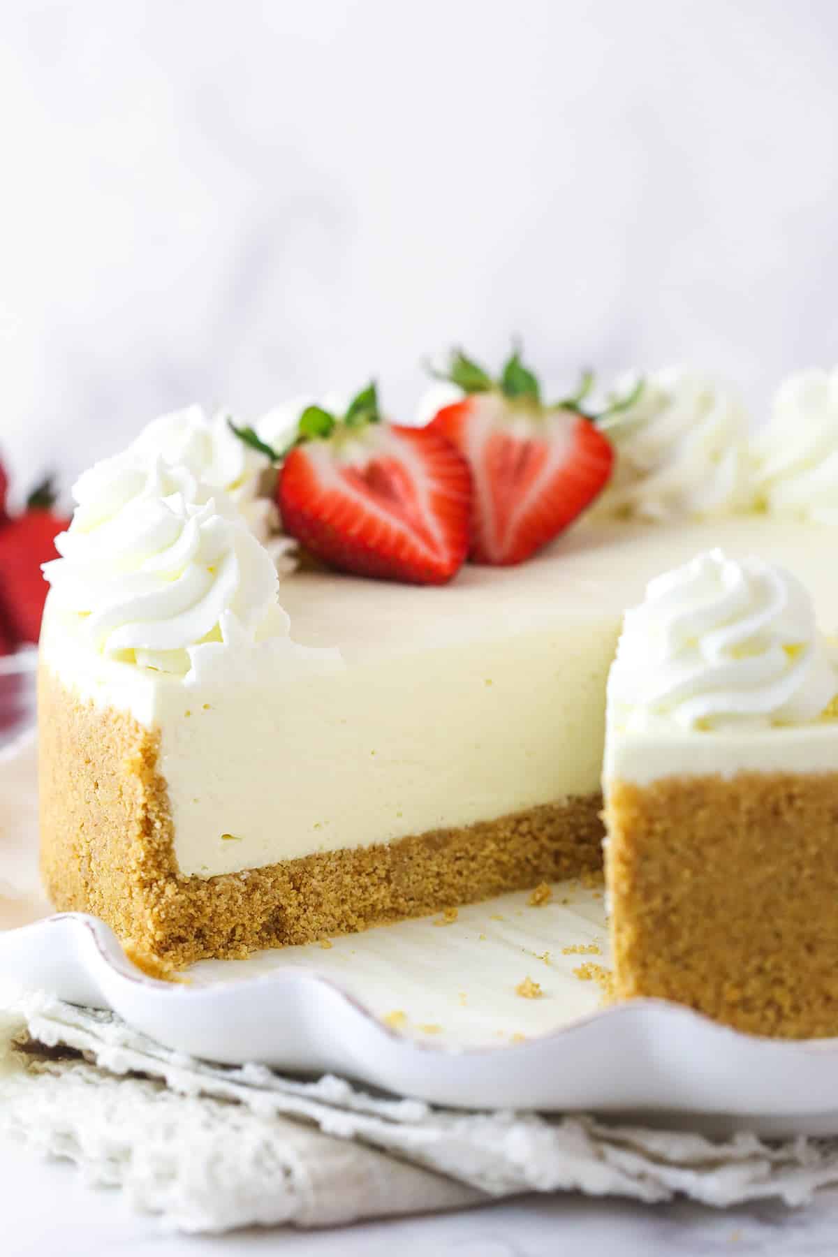 A whole no bake cheesecake on a serving platter with a slice taken out of it.