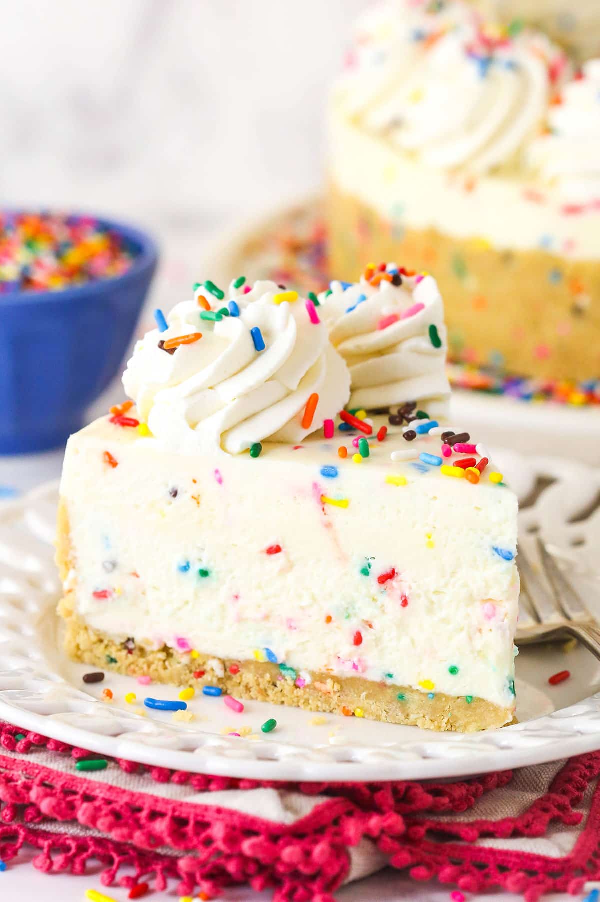 This No Bake Funfetti Cheesecake tastes like eating cake batter in cheesecake form. It's thick, creamy, and loaded with sprinkles. A slice of funfetti no bake cheesecake on a white plate