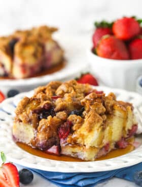A slice of berry French toast casserole served on a plate with maple syrup.