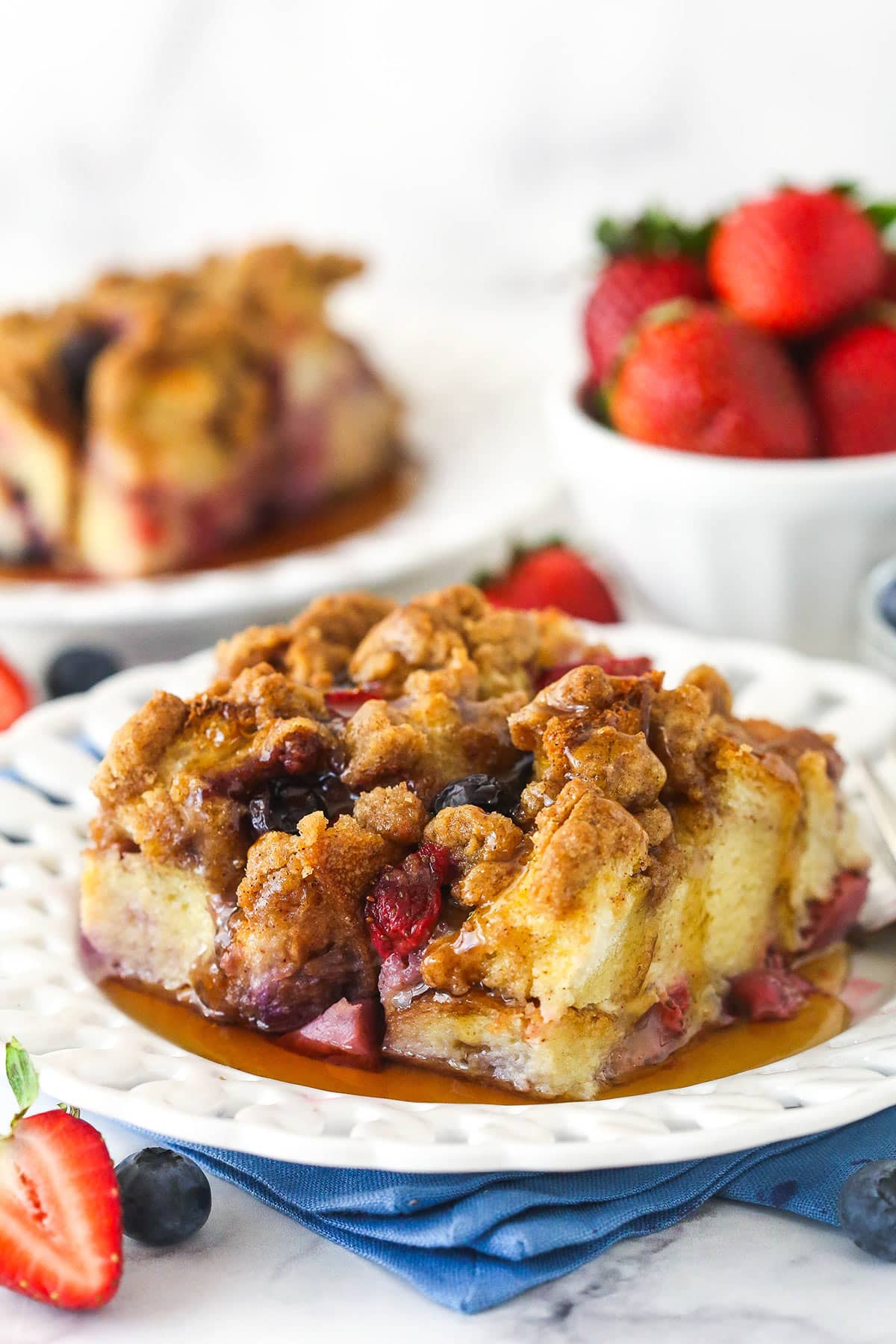 This make-ahead berry french toast casserole is loaded with flavorful pops of fresh fruit and topped with a buttery streusel topping. Wow! A slice of berry French toast casserole served on a plate with maple syrup.