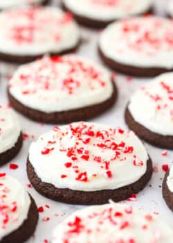 Several Peppermint Frosted Chocolate Cookies topped with candy cane bits on a flat surface.