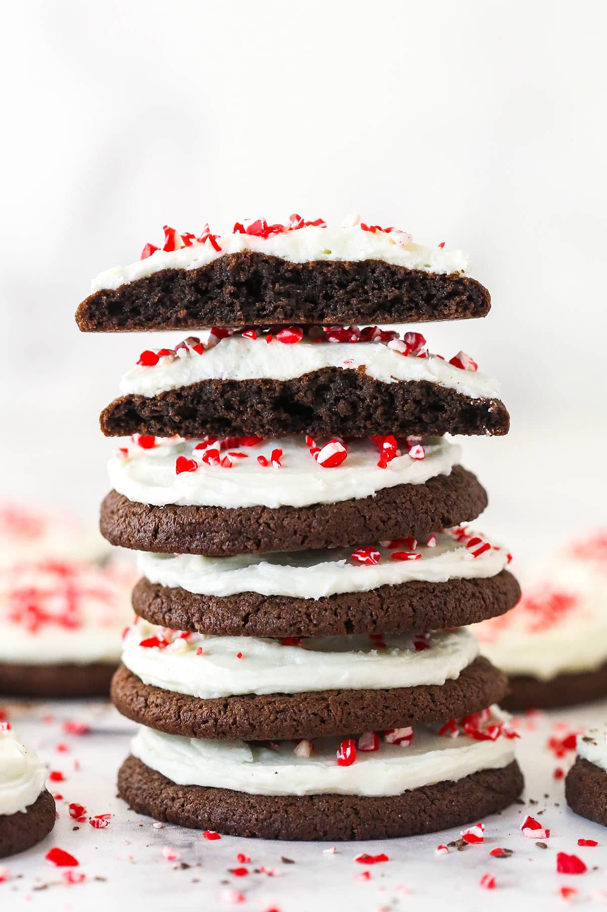 A stack of Peppermint Frosted Chocolate Cookies with the top cookie cut in half to show texture.