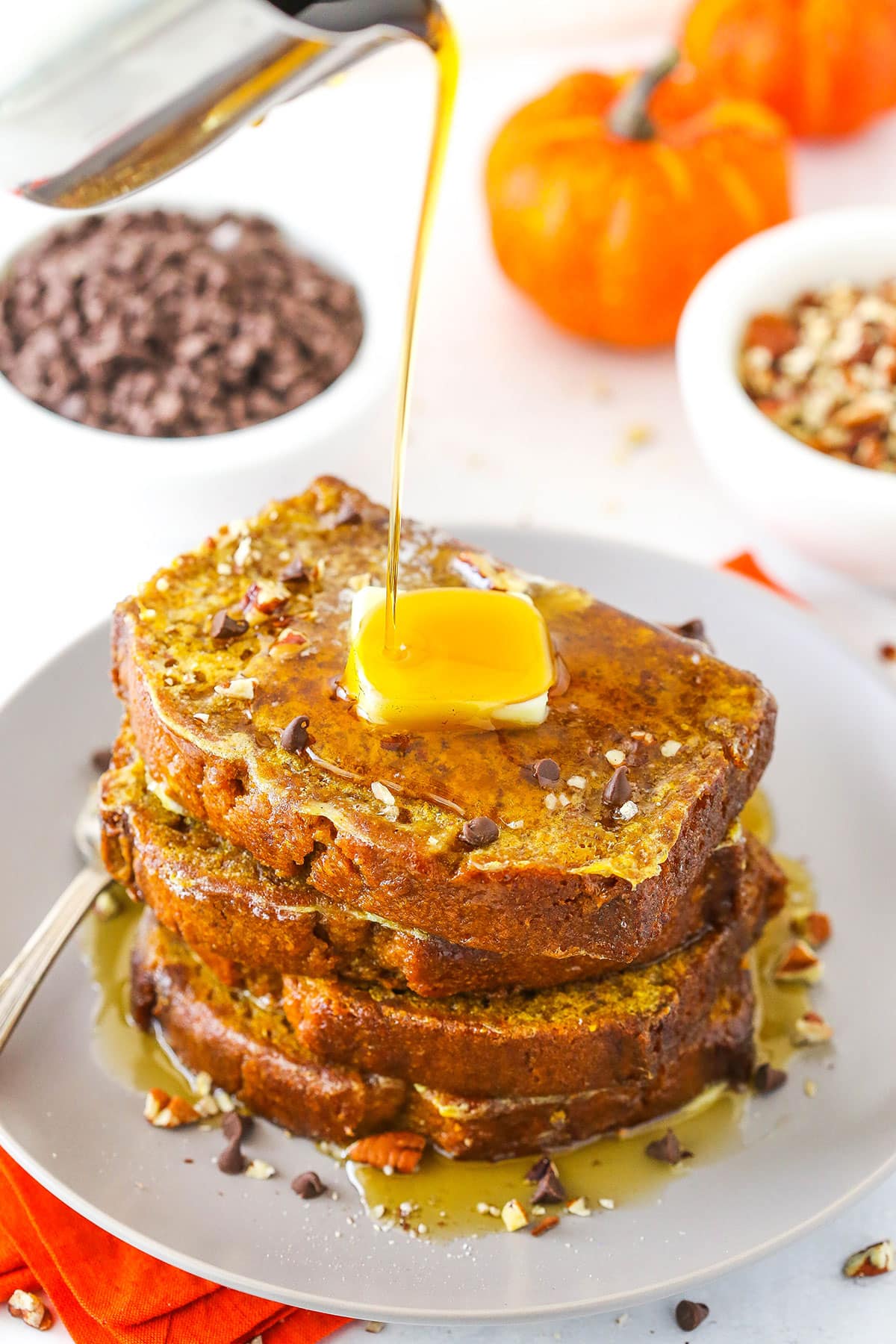 This Pumpkin Bread French Toast recipe is one seriously over-the-top breakfast that's totally worth it! Warm pumpkin bread with a crisp crust from cooking - it's truly amazing! Syrup being poured over four slices of Pumpkin Bread French Toast stacked on a white plate