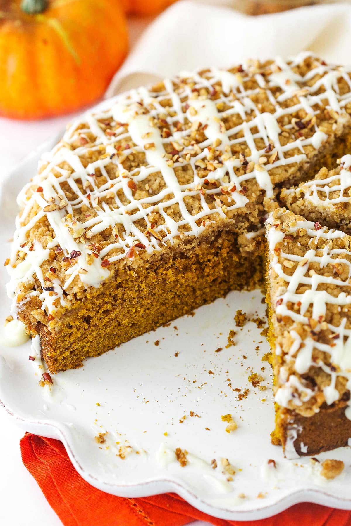 Complete with cinnamon streusel and a sweet vanilla glaze, this moist and fluffy pumpkin coffee cake is the perfect fall breakfast/dessert! A cinnamon streusel coffee cake on a cake platter with one big slice missing.