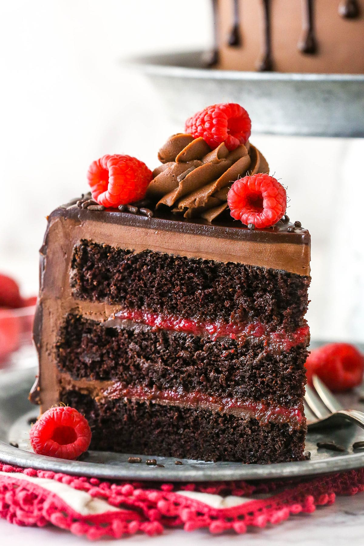 This chocolate raspberry cake is made of moist chocolate cake, smooth raspberry filling, dark chocolate frosting, and rich chocolate ganache. A slice of chocolate raspberry cake on a plate with a fork.