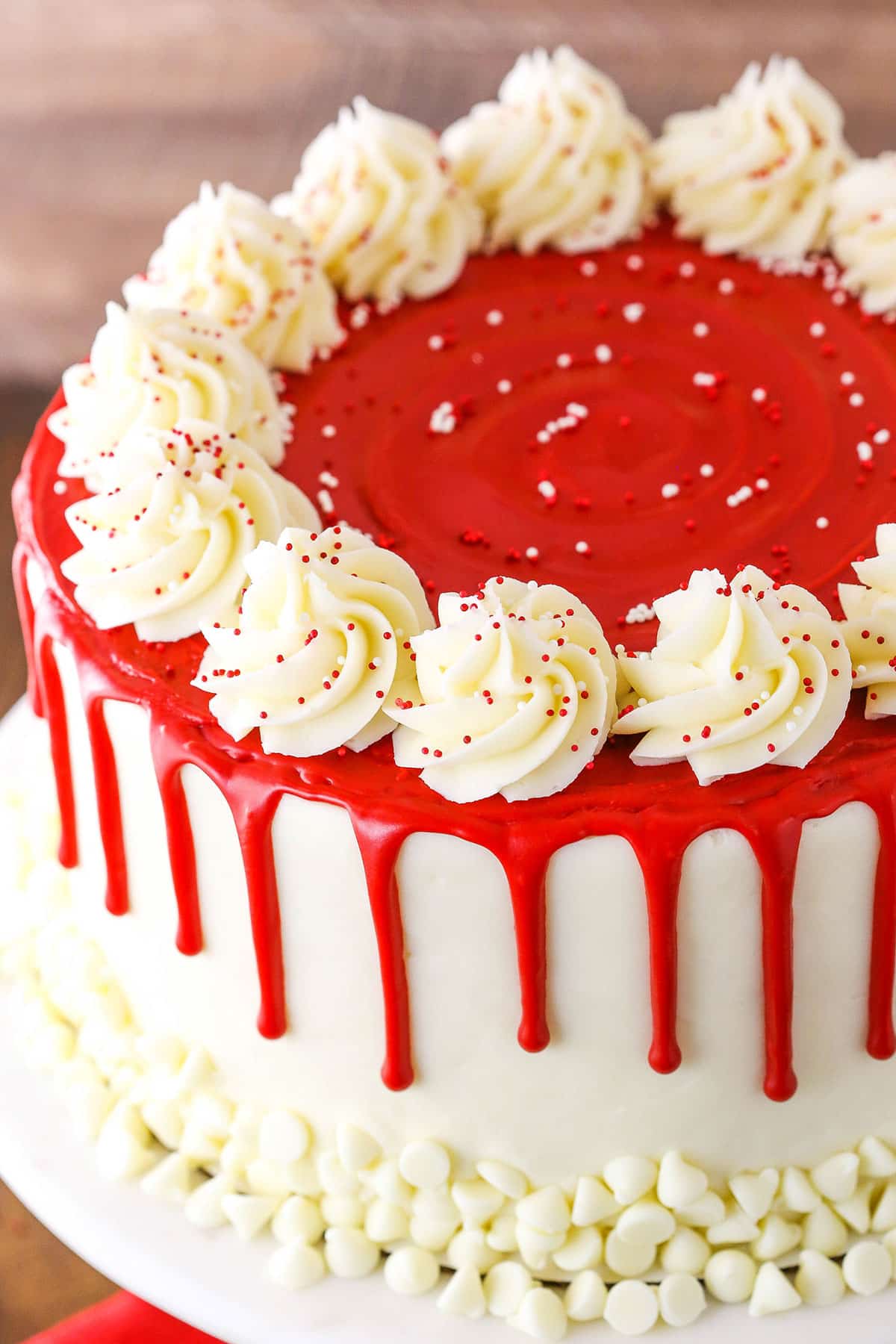 This Red Velvet Cheesecake Cake recipe has layers of moist red velvet cake and creamy cheesecake, covered in cream cheese frosting! If you've ever had the cheesecake by the same name at The Cheesecake Factory and loved it, this is the perfect recipe to make at home! Overhead view of a full Red Velvet Cheesecake Cake on a white cake stand