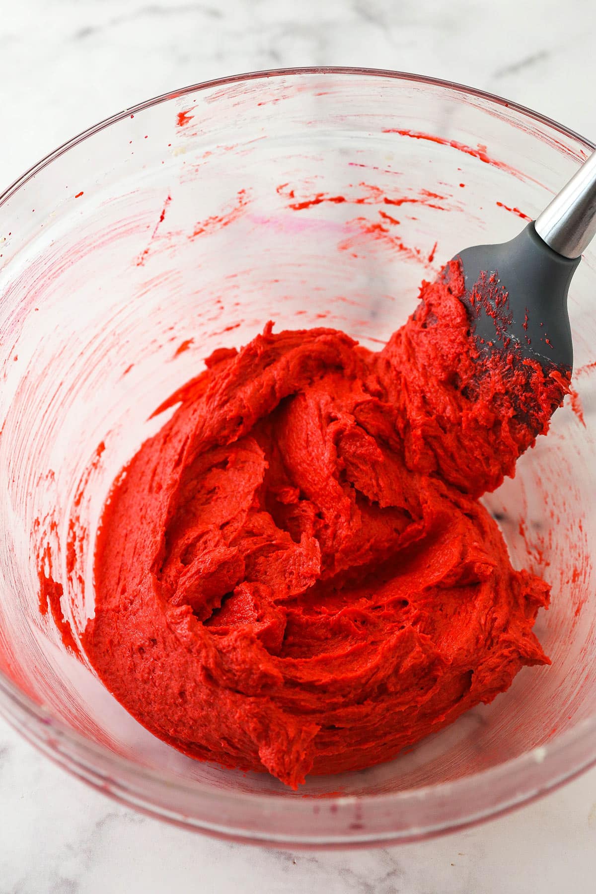 Cookie dough colored with red food dye in a glass bowl with a spatula.