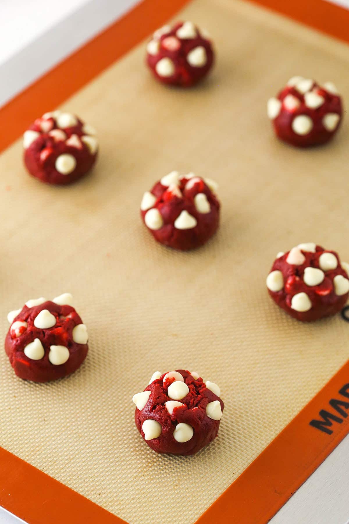 Rolled cookie dough balls on a cookie sheet lined with a silicone baking mat.