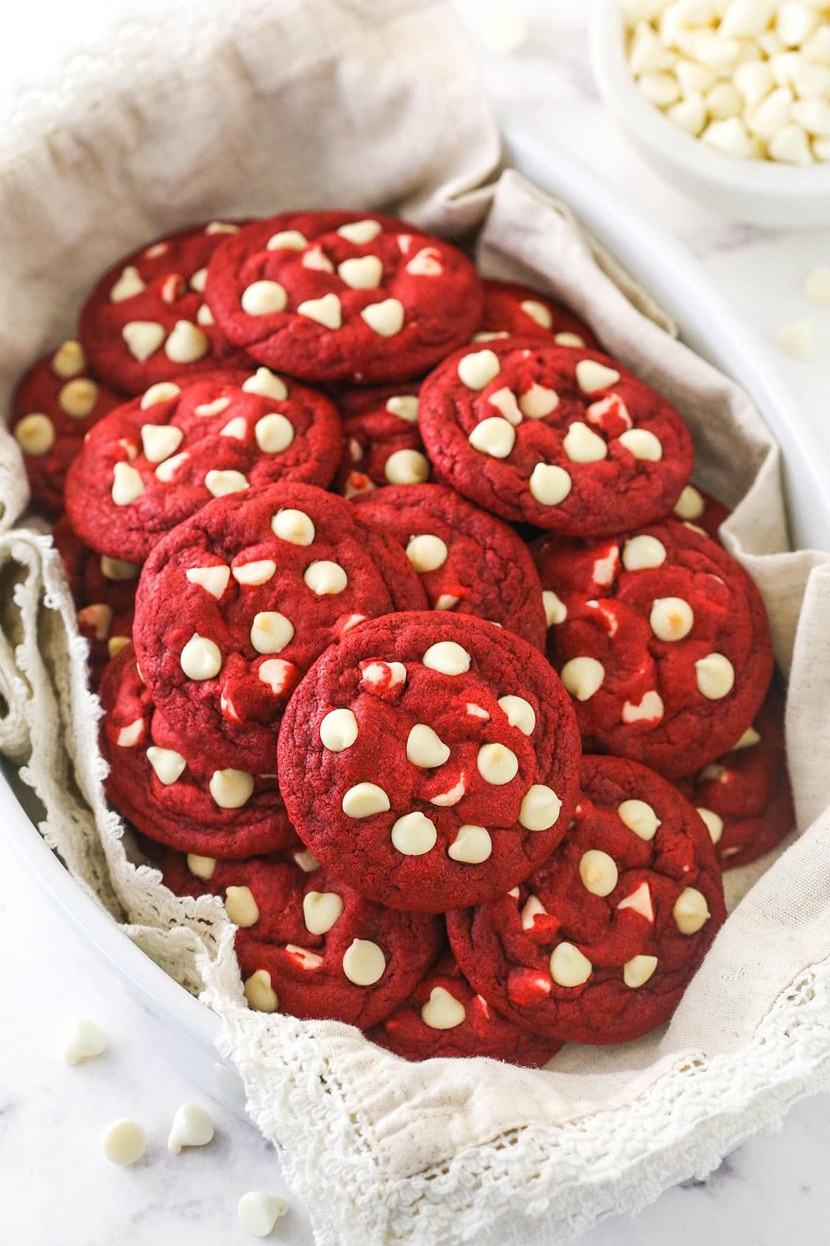 Red velvet cookies with white chocolate chips in a container lined with a white cloth.