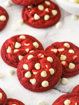 Angled shot of three red velvet cookies with white chocolate chips, with more cookies in the background.