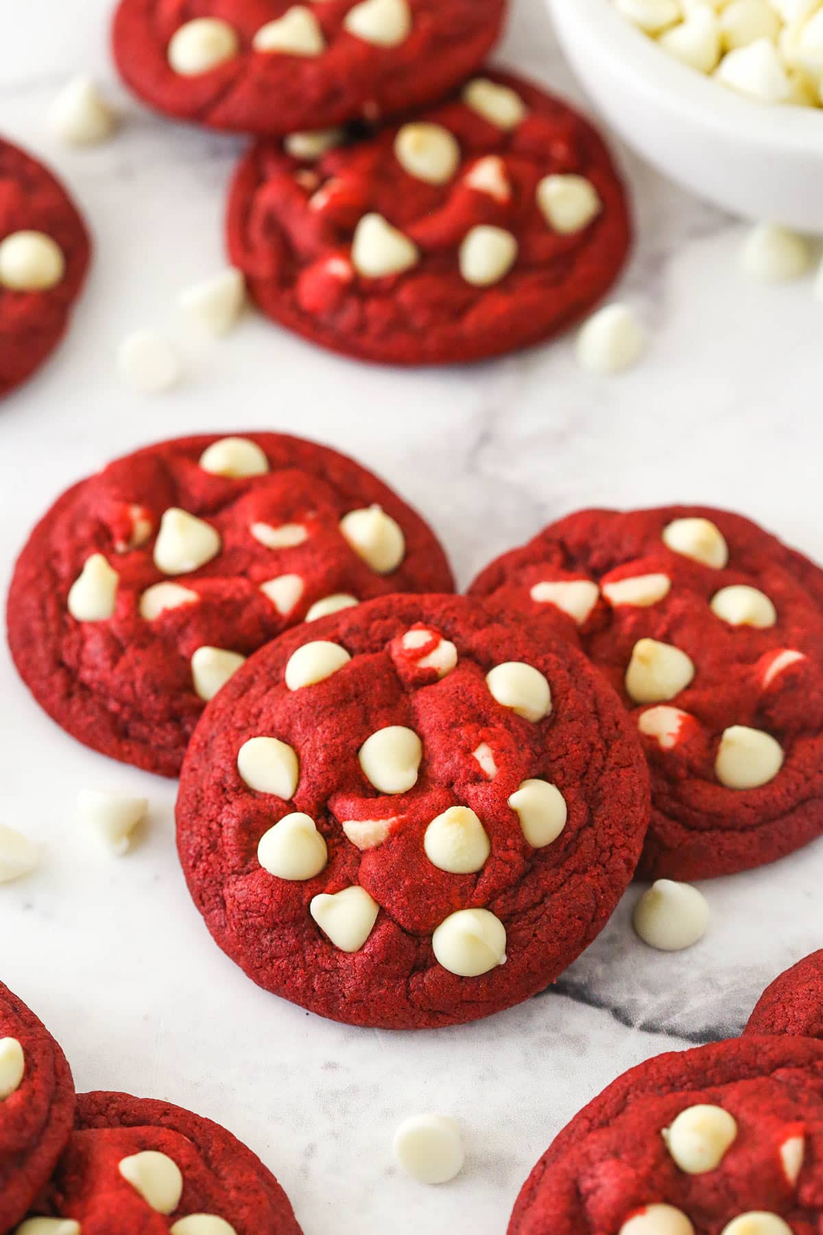 Angled shot of three red velvet cookies with white chocolate chips, with more cookies in the background.