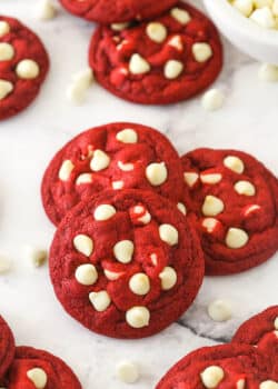 Angled shot of three red velvet cookies with white chocolate chips, with more cookies in the background.