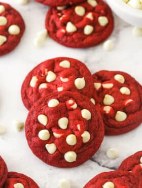 Angled shot of three red velvet cookies with white chocolate chips, with more cookies in the background.