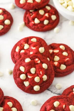 Angled shot of three red velvet cookies with white chocolate chips, with more cookies in the background.