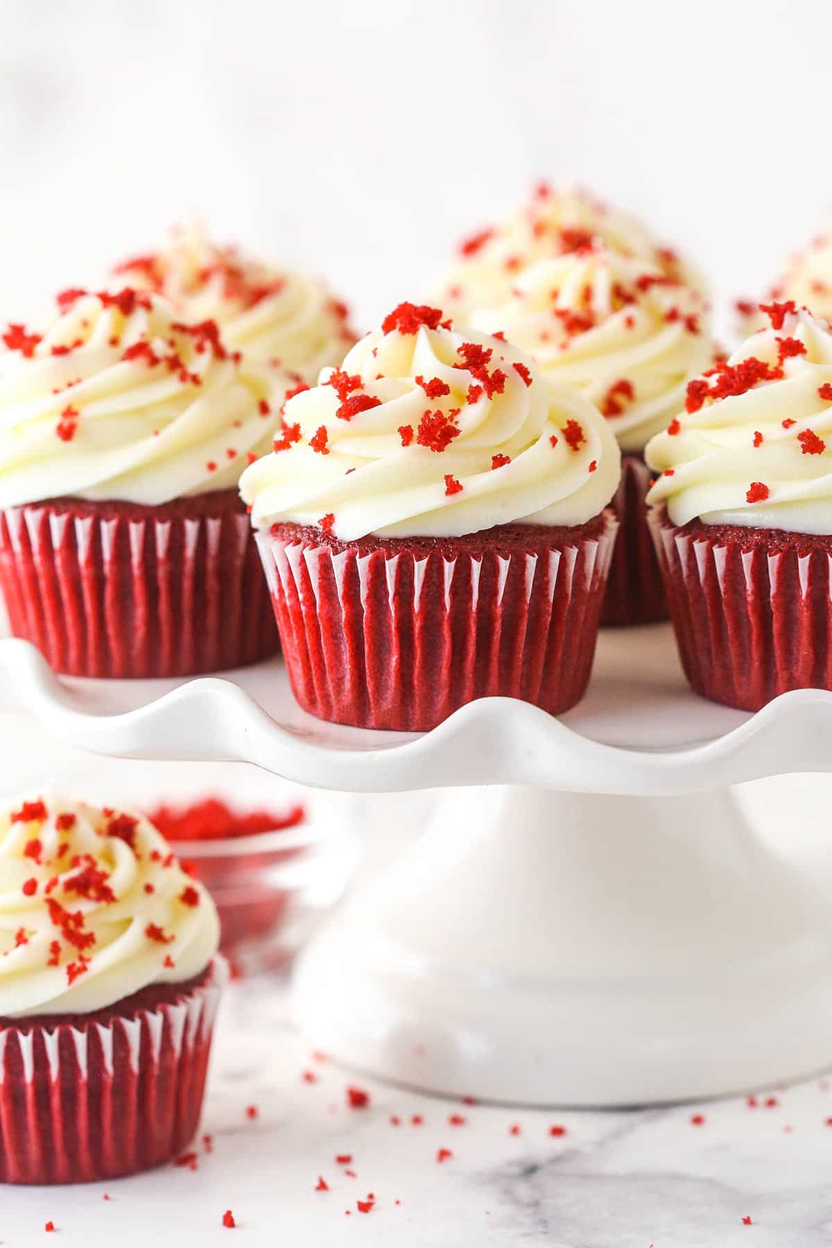 Moist, tender, and somewhere between chocolate and vanilla with decadent cream cheese frosting, red velvet cupcakes are a dessert miracle. Red velvet cupcakes on a cake stand.