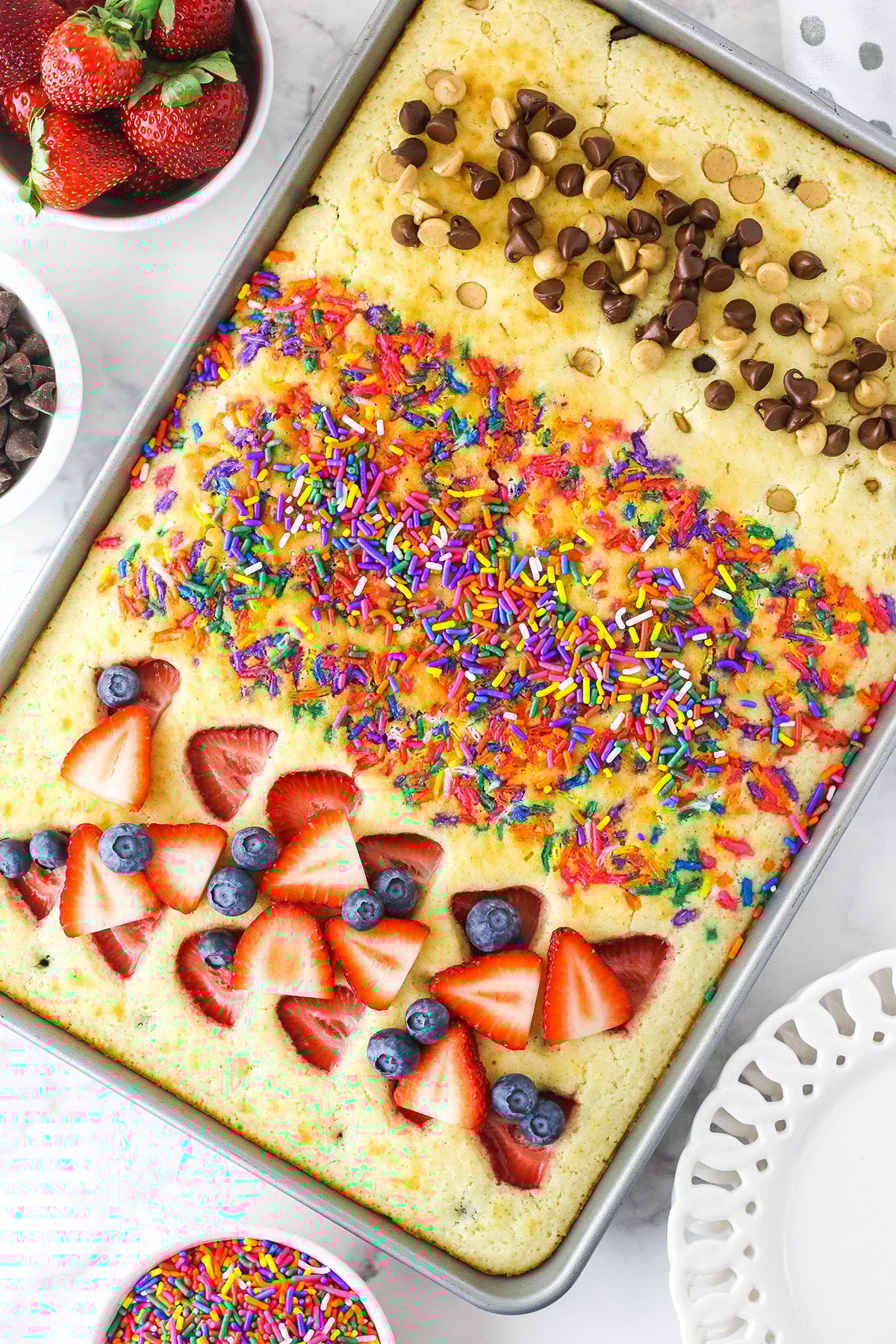 A sheet pan full of cooked pancakes with fruit, sprinkles and chocolate & peanut butter chips on top