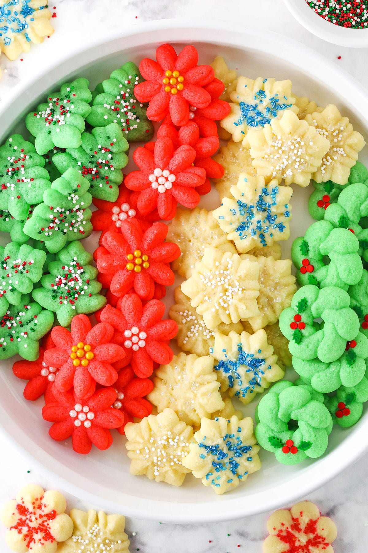 These Spritz Cookies are buttery, tender and such festive Christmas cookies! The cookie dough is super easy to put together and there's so many ways to decorate them. A great make-ahead cookie! Red flower, white snowflake and green Christmas tree Spritz Cookies layered in a white cookie platter