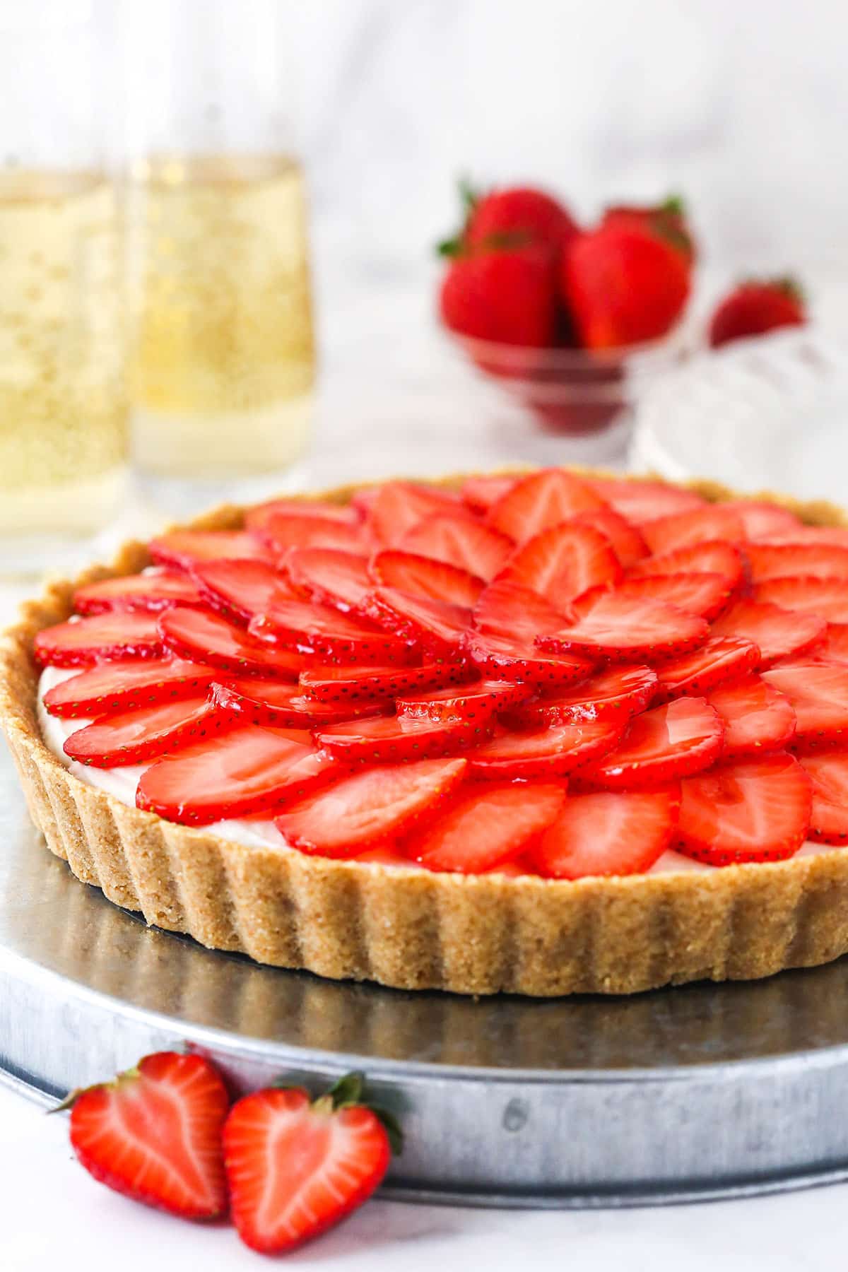 A wafer crust surrounds a creamy champagne mascarpone tart filling, topped with juicy strawberry slices, to create the best strawberry tart! strawberry champagne tart on silver platter