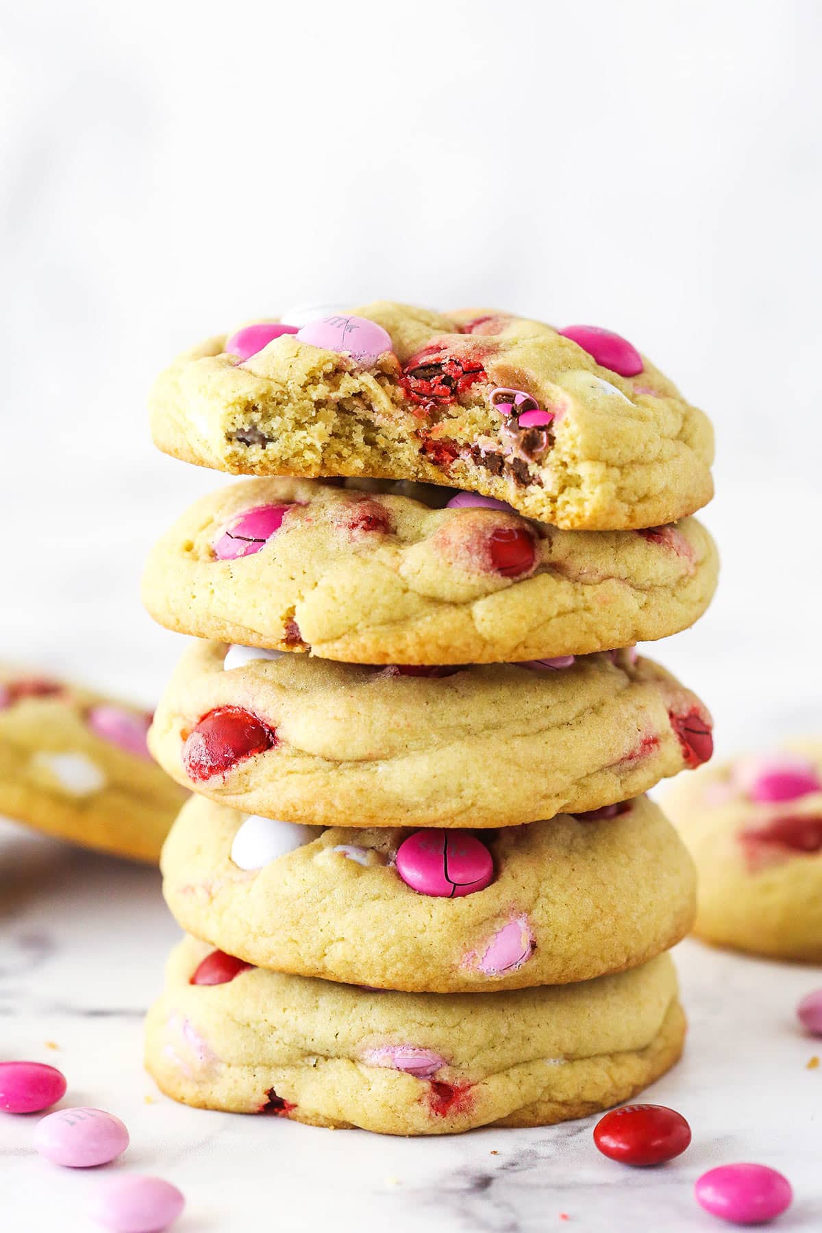 Thick, chewy, and loaded with red, pink, and white M&Ms, these Valentine's Day M&M cookies are sure to win over the hearts and taste. A stack of Valentine's Day M&M cookies. The top cookie has a bite taken out of it.